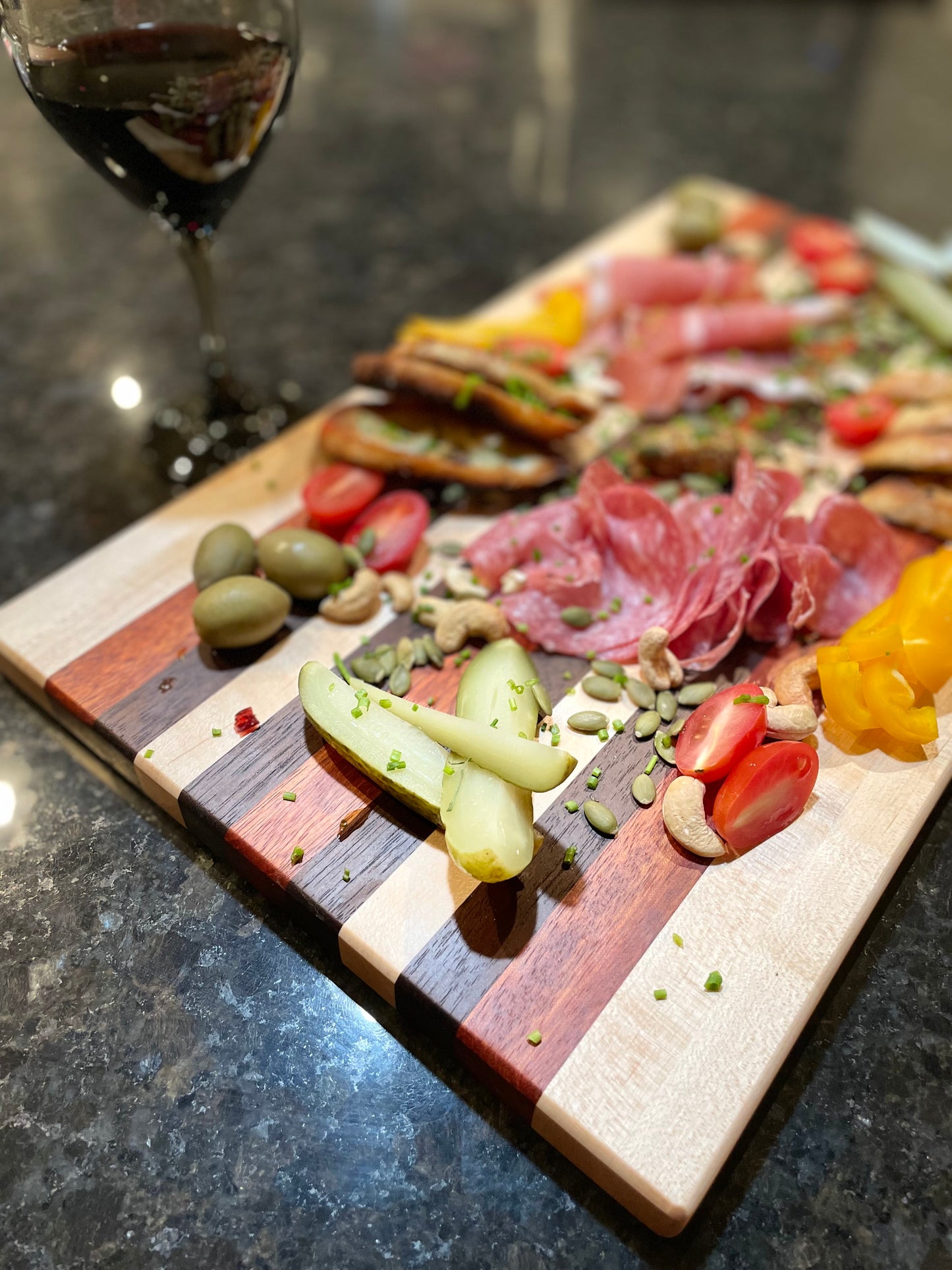 custom edge grain charcuterie red zebrawood maple walnut, side/top view, cured meats, vegetables, olives and a glass of red wine.