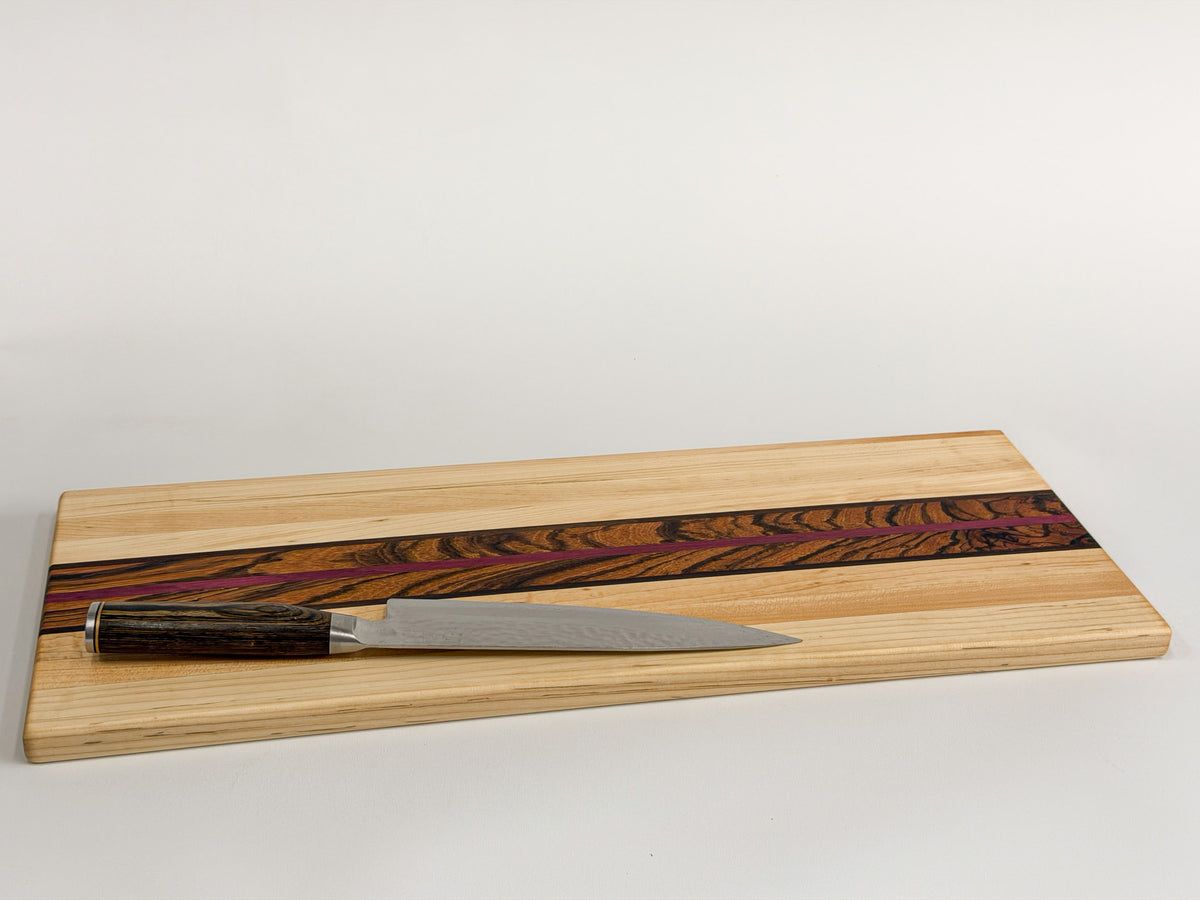 Zephyr maple cutting board with zebrawood and purpleheart accents displayed with a chef’s knife.