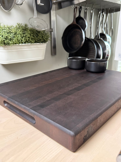 Wooden end grain walnut cutting board on a kitchen counter with pots and pans in the background