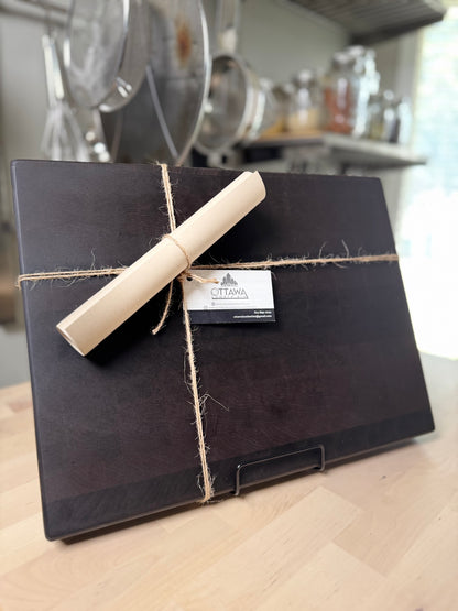Black string-bound cutting board with rolled-up instructions tied with twine on a kitchen counter.