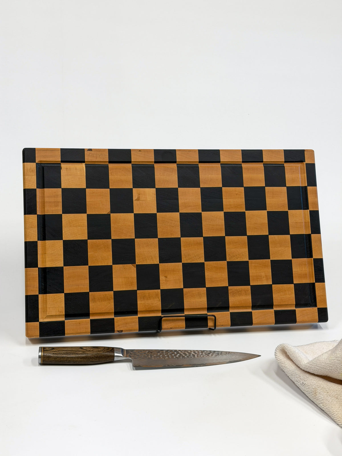 Checkerboard end-grain cutting board displayed with a chef’s knife and white towel.