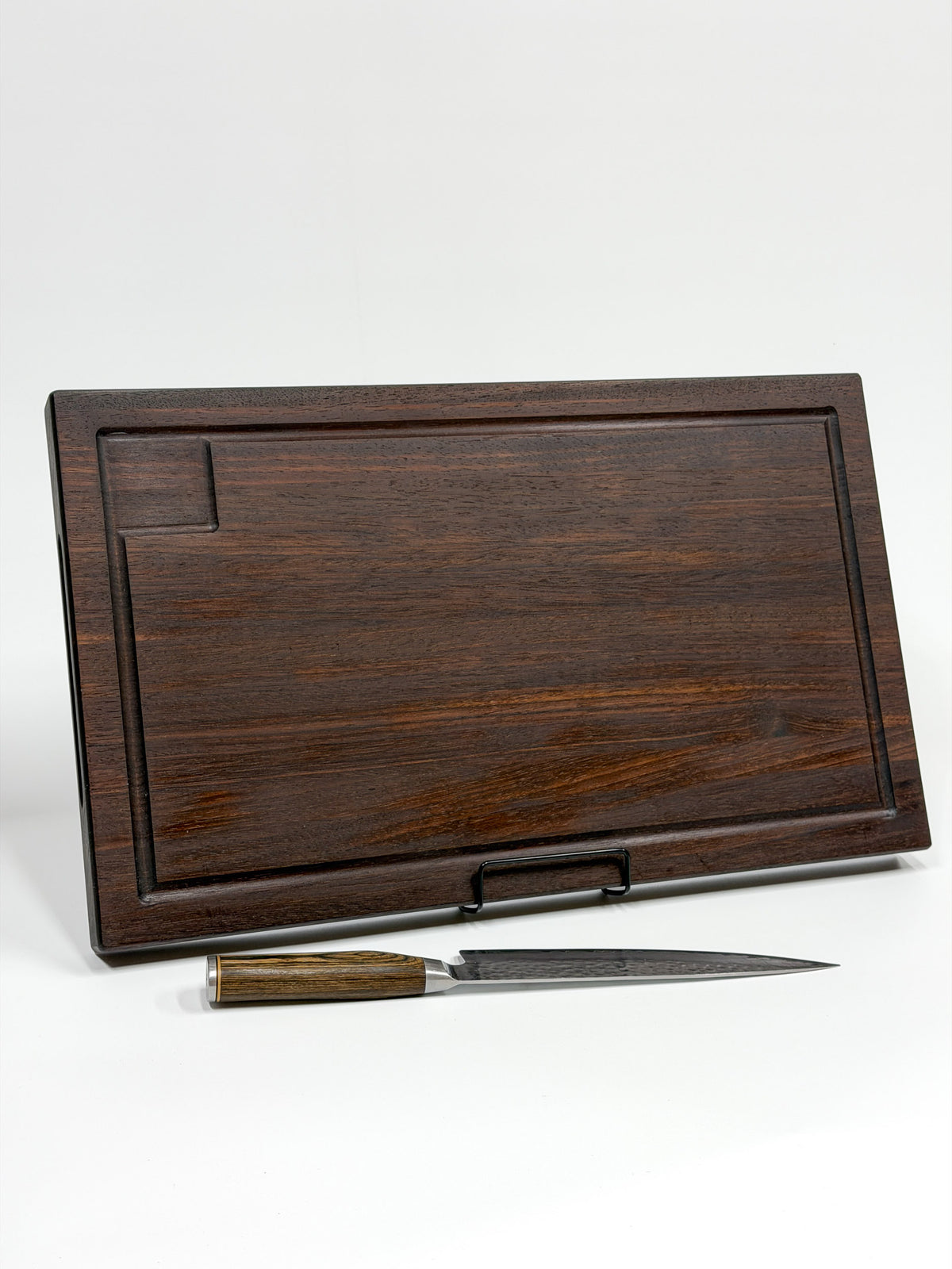 Dark walnut wood carving board with a juice groove, displayed with a chef’s knife.