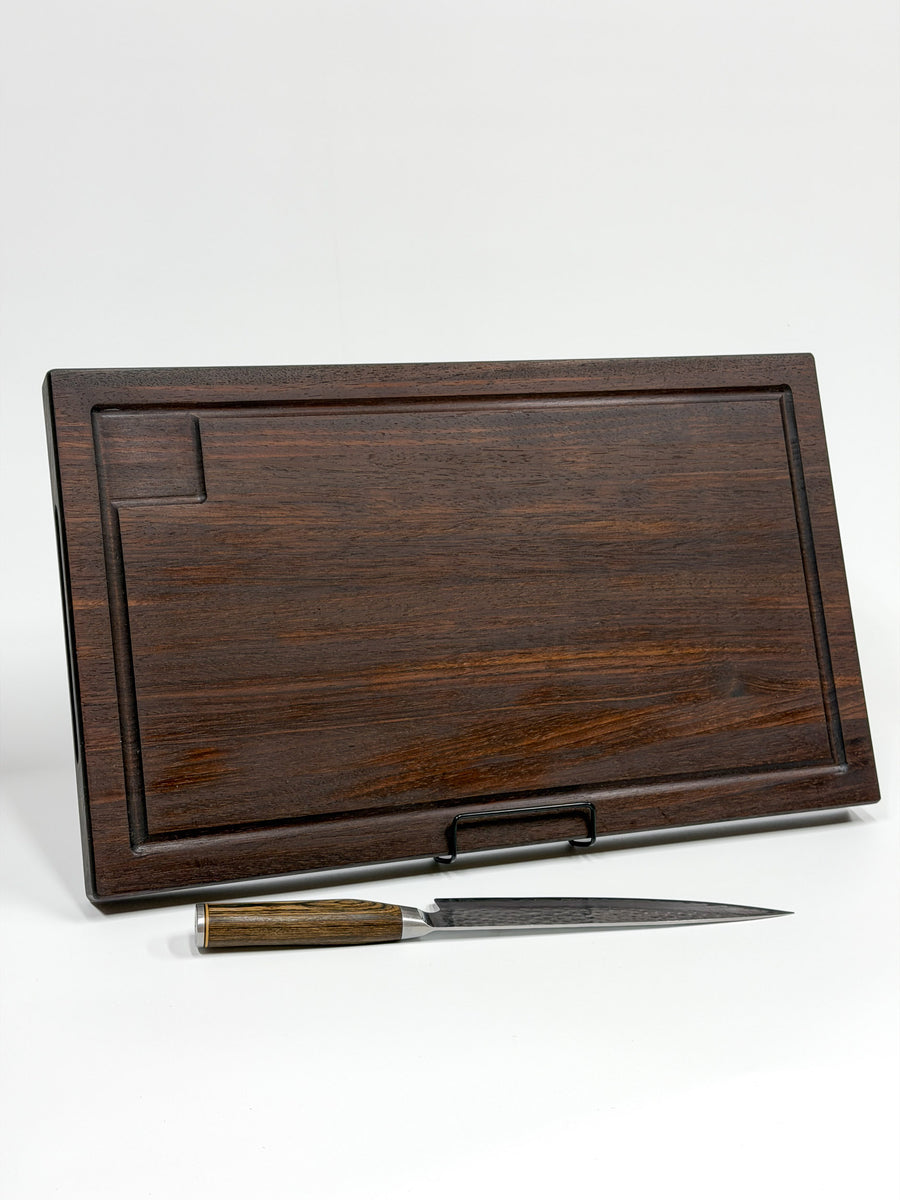 Dark walnut wood carving board with a juice groove, displayed with a chef’s knife.