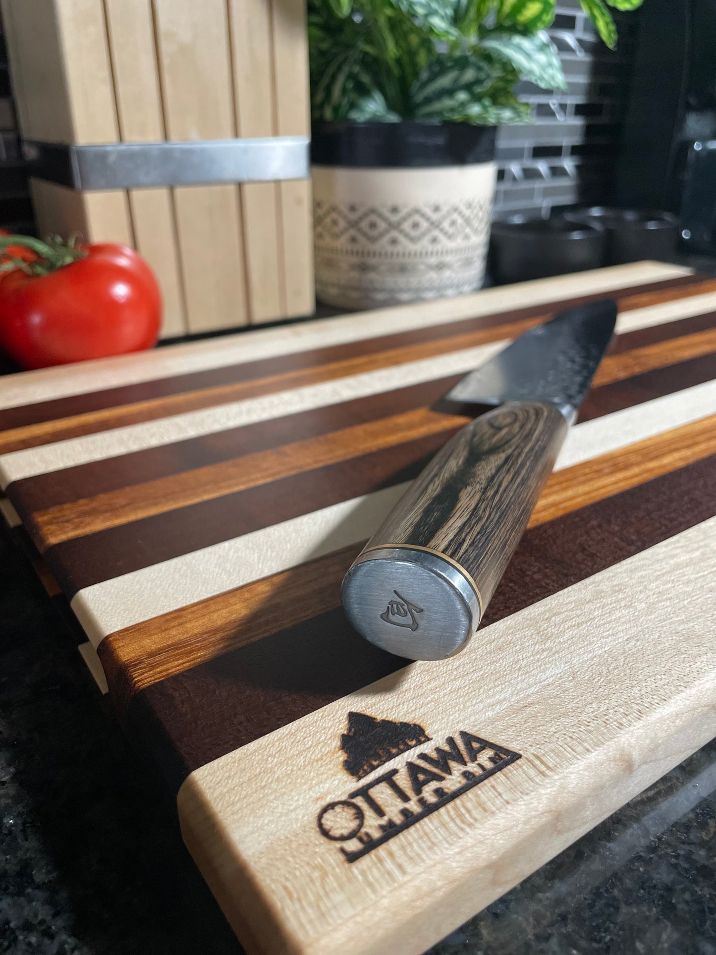 Edge grain charcuterie board made from maple, walnut and tigerwood displayed with a cheese knife.