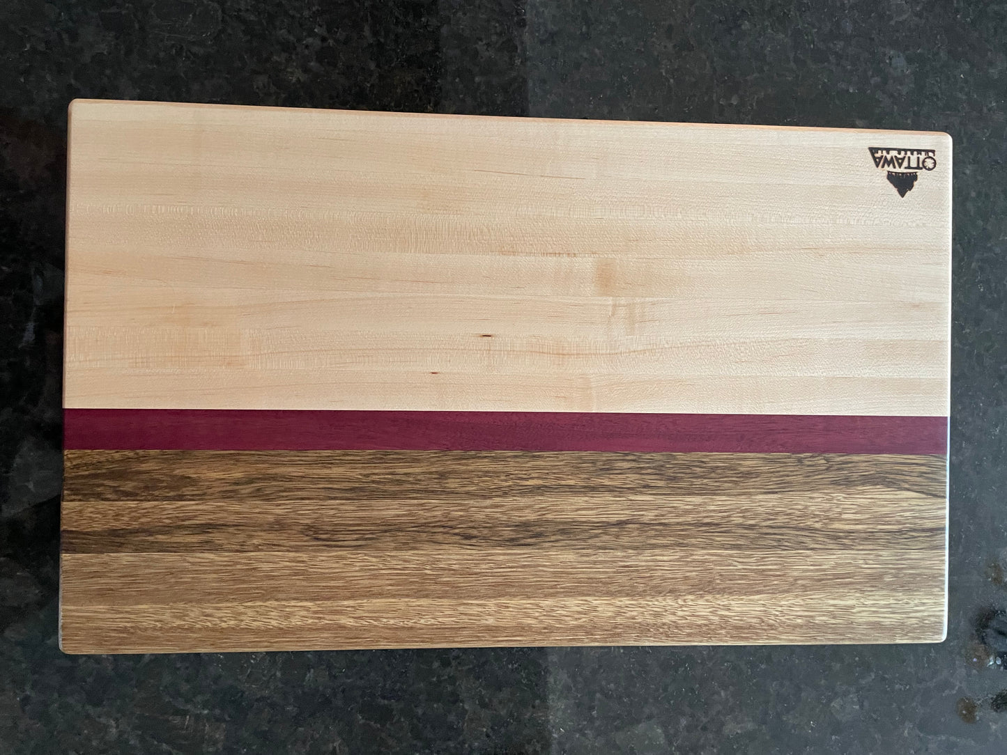 Close-up of a handcrafted edge grain charcuterie board showcasing maple, black limba and Purpleheart.