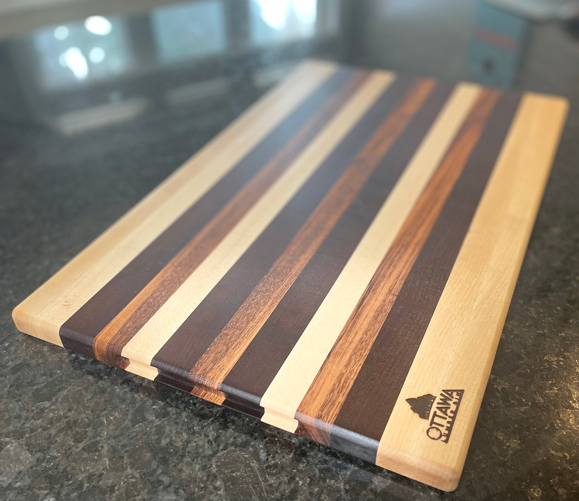 Top view of an edge grain charcuterie board featuring maple, walnut and tigerwood stripes.