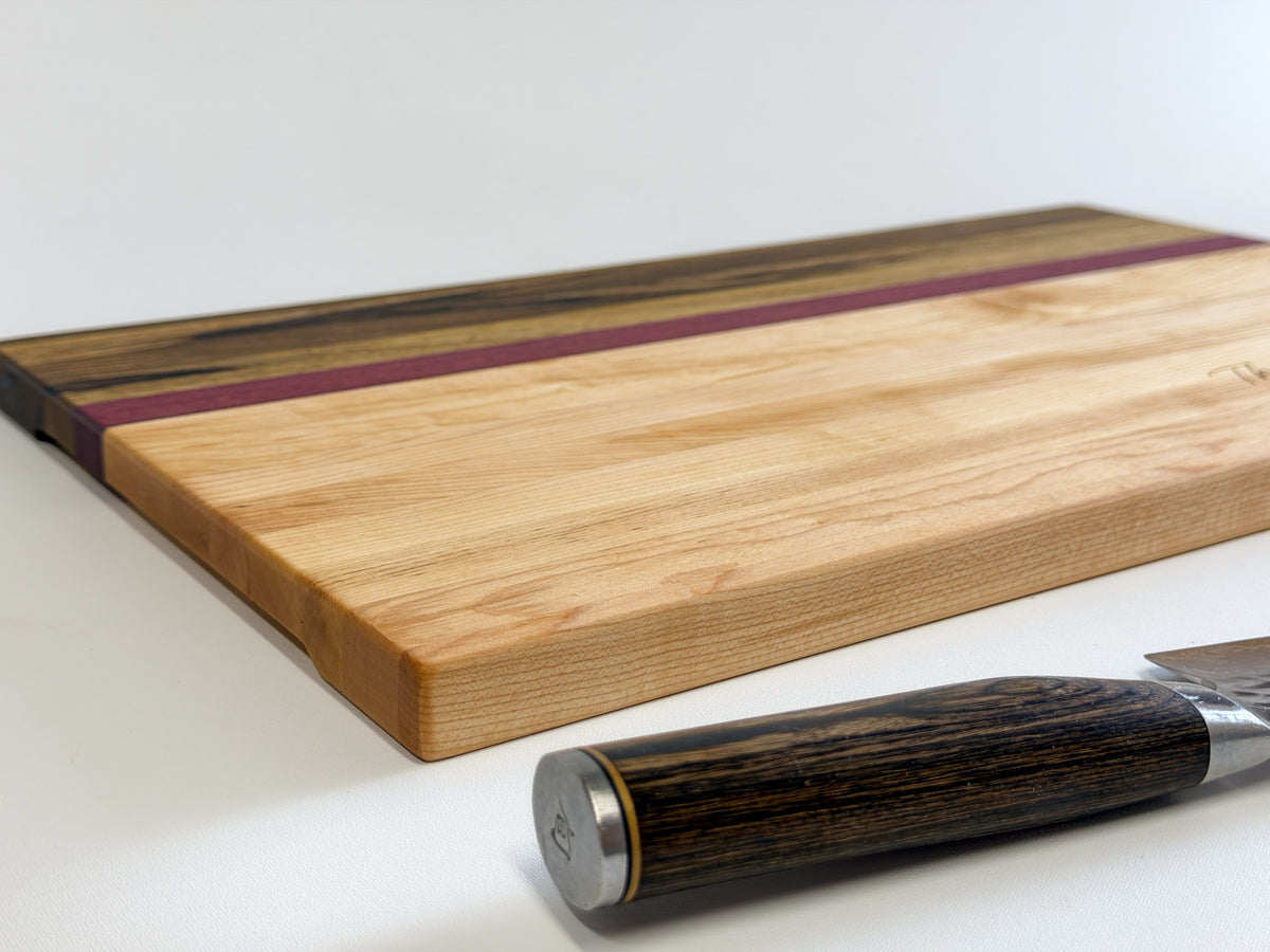 Close-up of a maple, purpleheart and black limba charcuterie board showing its contrasting wood grain and finished edge.