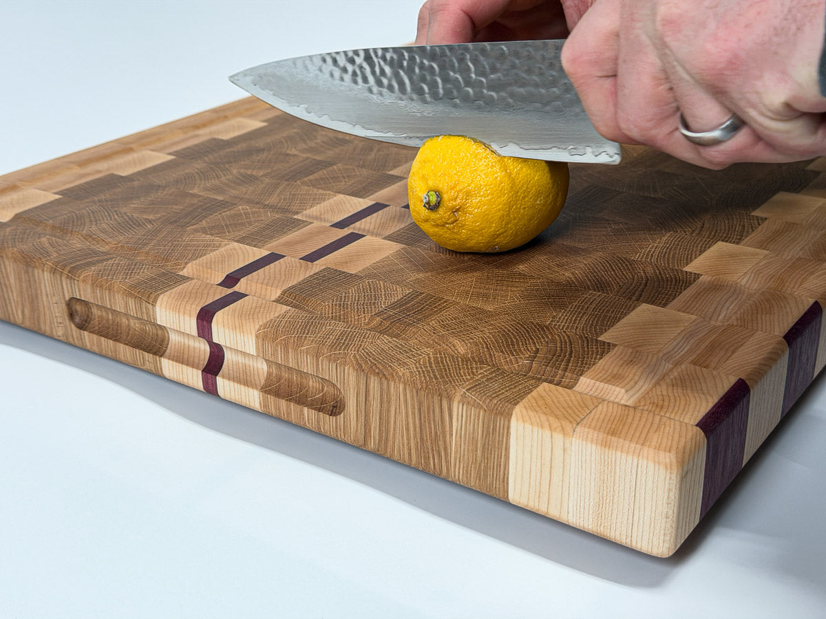 Chef slicing a lemon on a handcrafted end grain cutting board made from maple, white oak and Purpleheart.