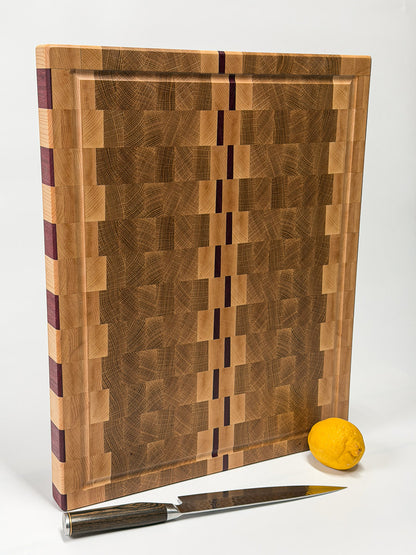 Standing end grain cutting board handcrafted from maple, white oak and Purpleheart with a juice groove, displayed with a chef's knife and lemon.
