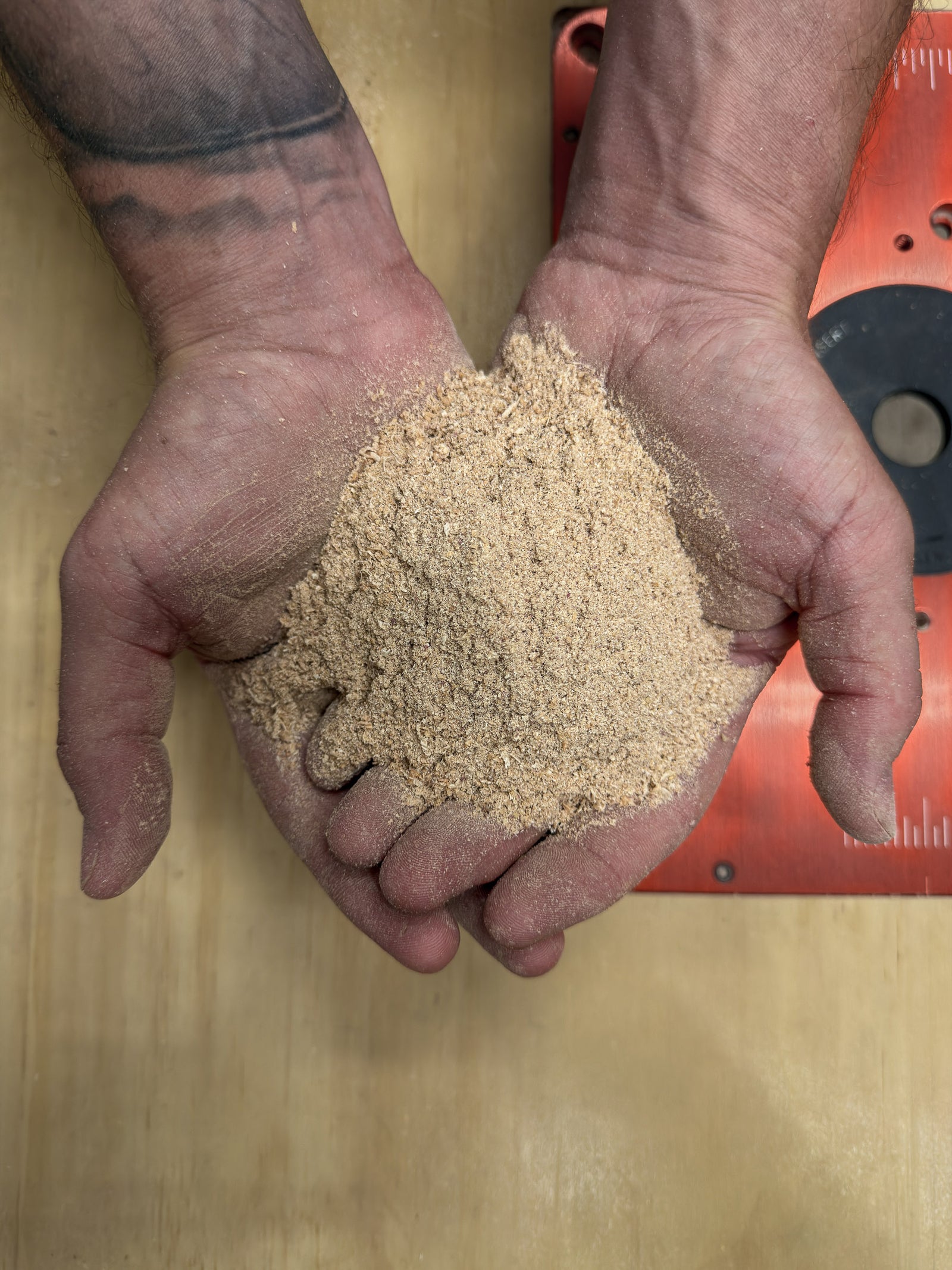 Woodworker holding a handful of sawdust in the workshop, representing the hands-on craftsmanship behind every handmade piece.