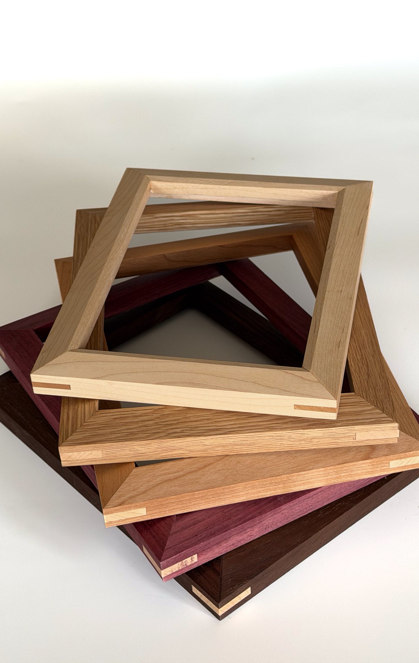 Stacked handcrafted hardwood picture frames showcasing five wood species including maple, walnut, white oak, cherry and purpleheart.