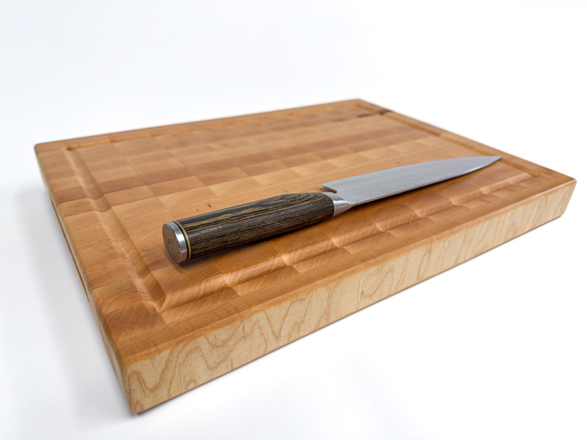 Langford maple end grain cutting board photographed with a chef’s knife across its patterned cutting surface