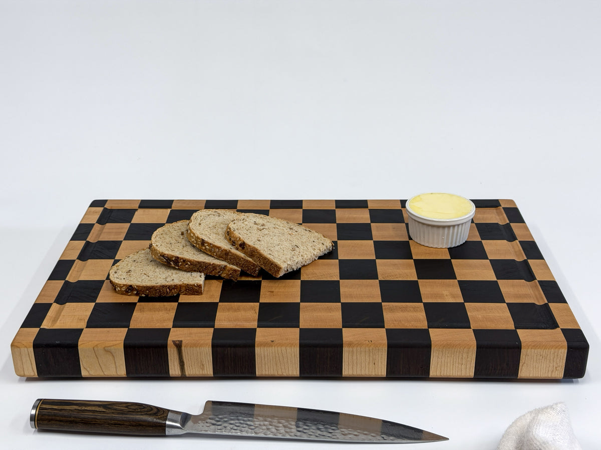 Large maple checkerboard cutting board styled with sliced bread, butter and a chef’s knife.