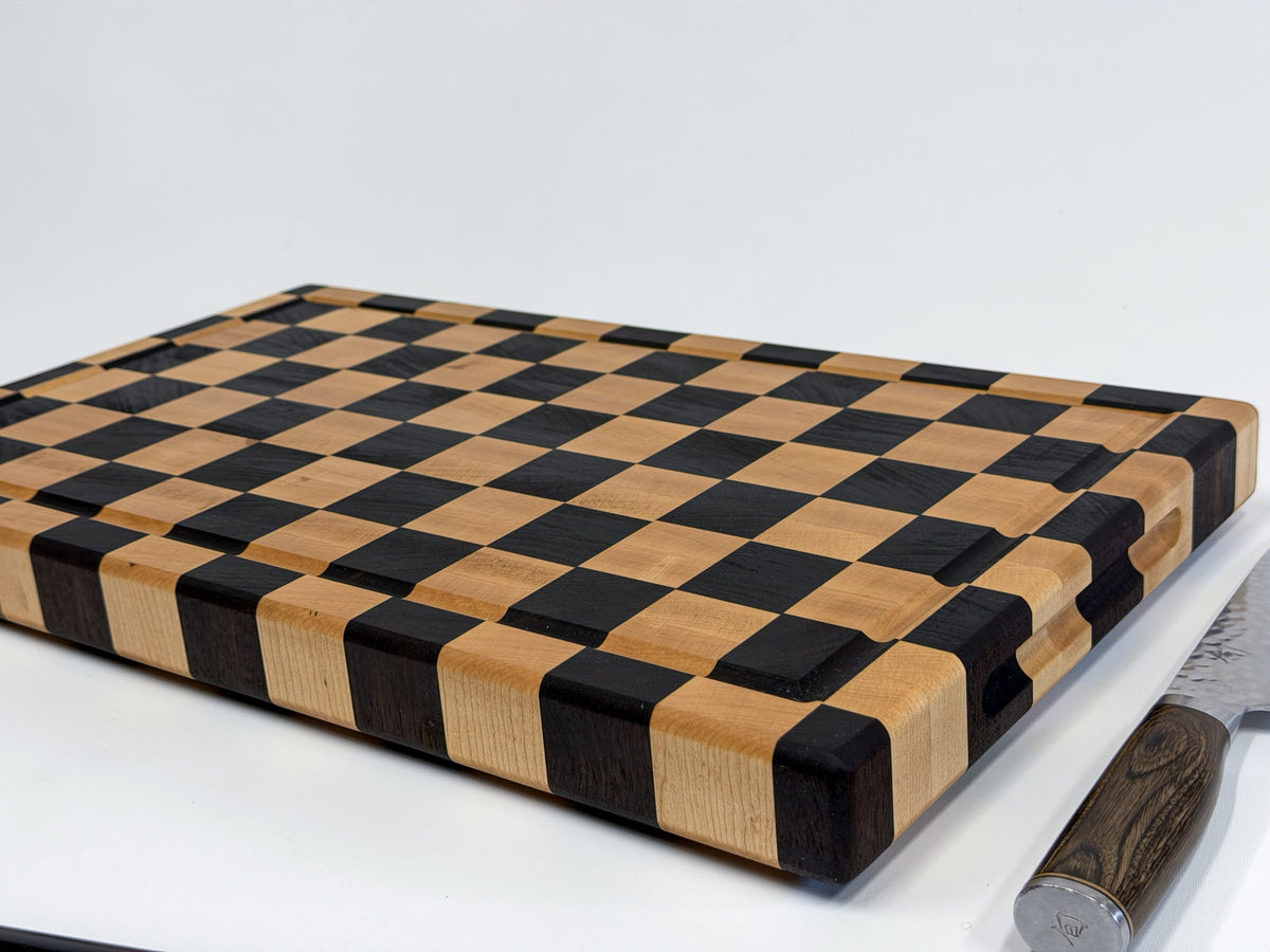 Low-angle view of a handcrafted maple checkerboard cutting board showing its thick edge and juice groove.