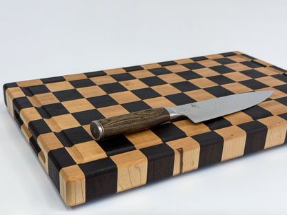 Handcrafted maple checkerboard cutting board with a chef’s knife resting across its grooved surface.
