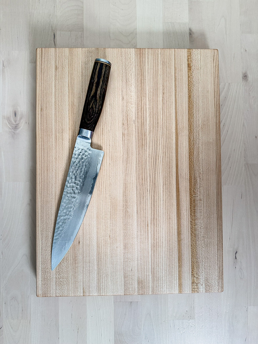 Overhead view of a handcrafted maple edge grain cutting board with a chef's knife.