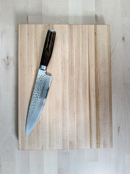 Overhead view of a handcrafted maple edge grain cutting board with a chef's knife.
