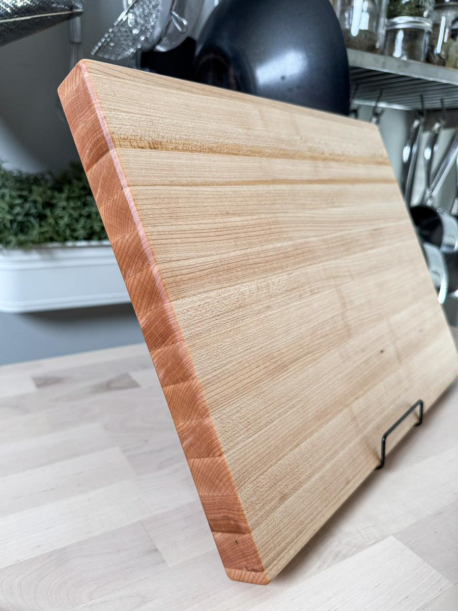 Handcrafted maple edge grain cutting board shown standing at an angle.