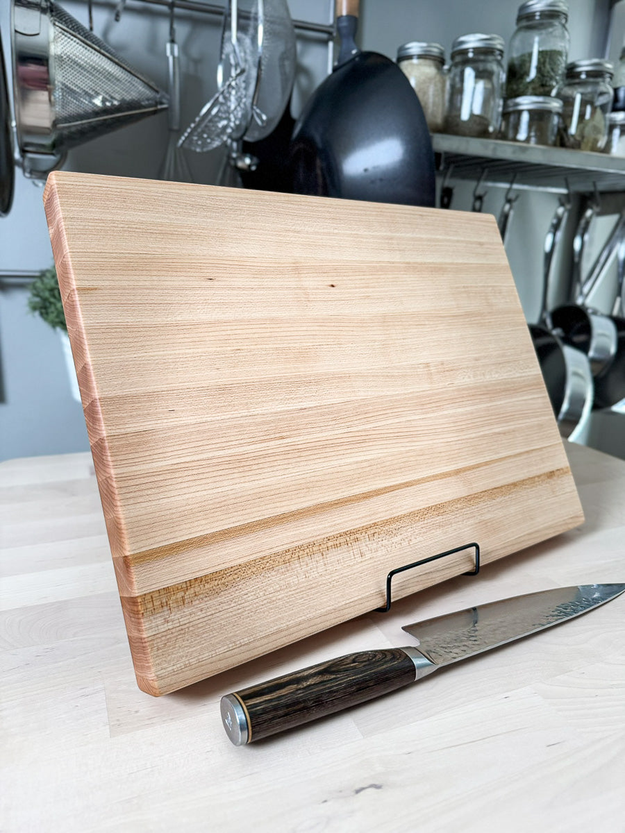 Standing handcrafted maple edge grain cutting board displayed with a chef's knife.