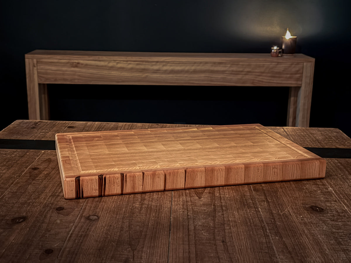 End-grain maple cutting board displayed on a dining table with candles glowing in the background.