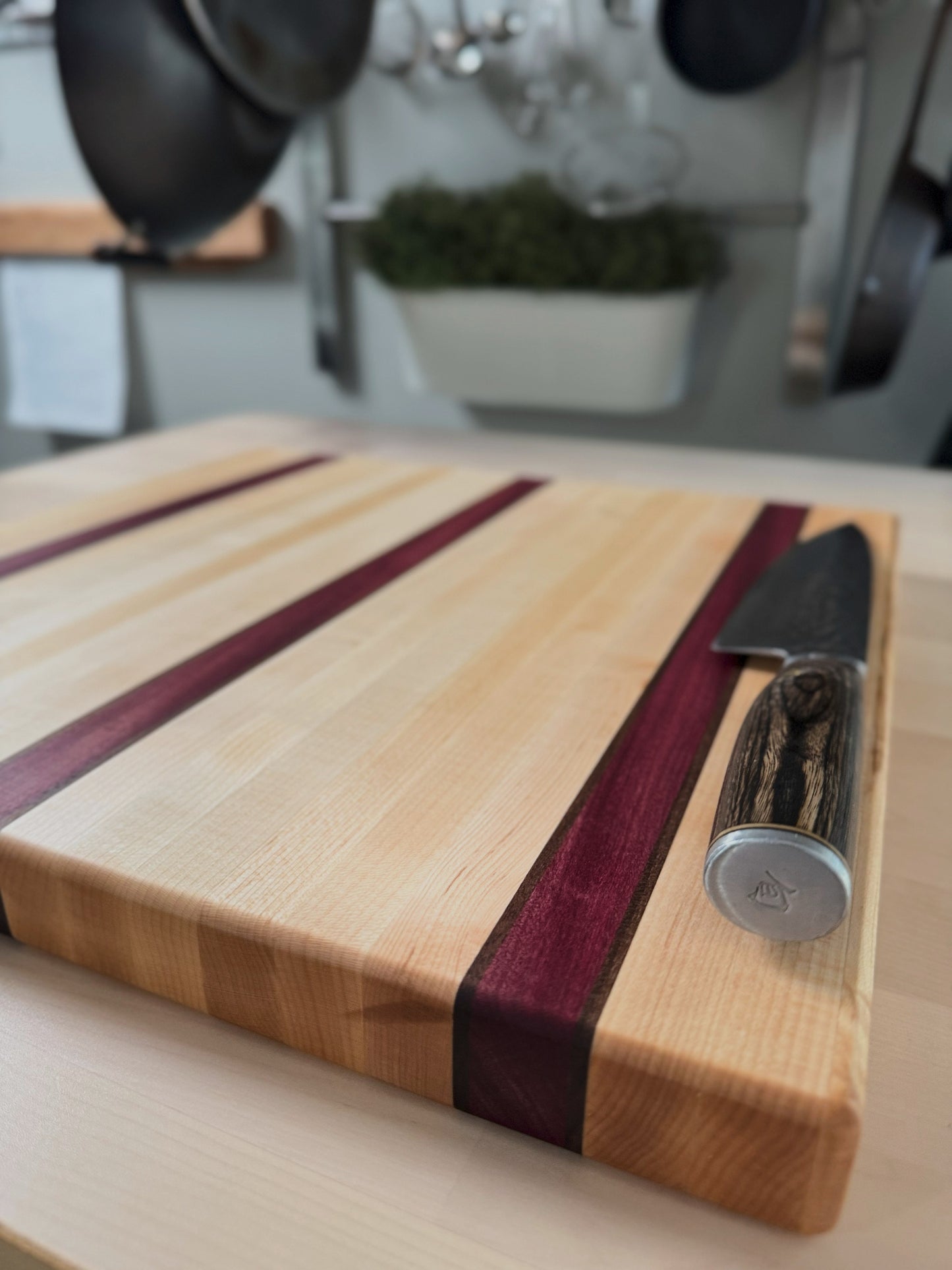 Angled view of a maple edge grain cutting board featuring Purpleheart and walnut accent stripes.