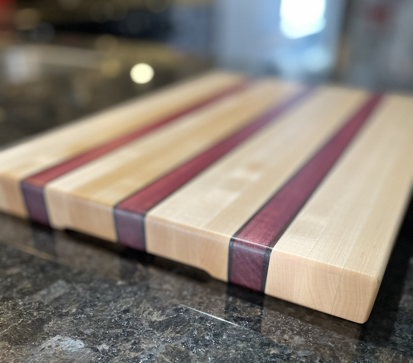 Close-up of a handcrafted maple edge grain cutting board showcasing Purpleheart and walnut accent stripes.