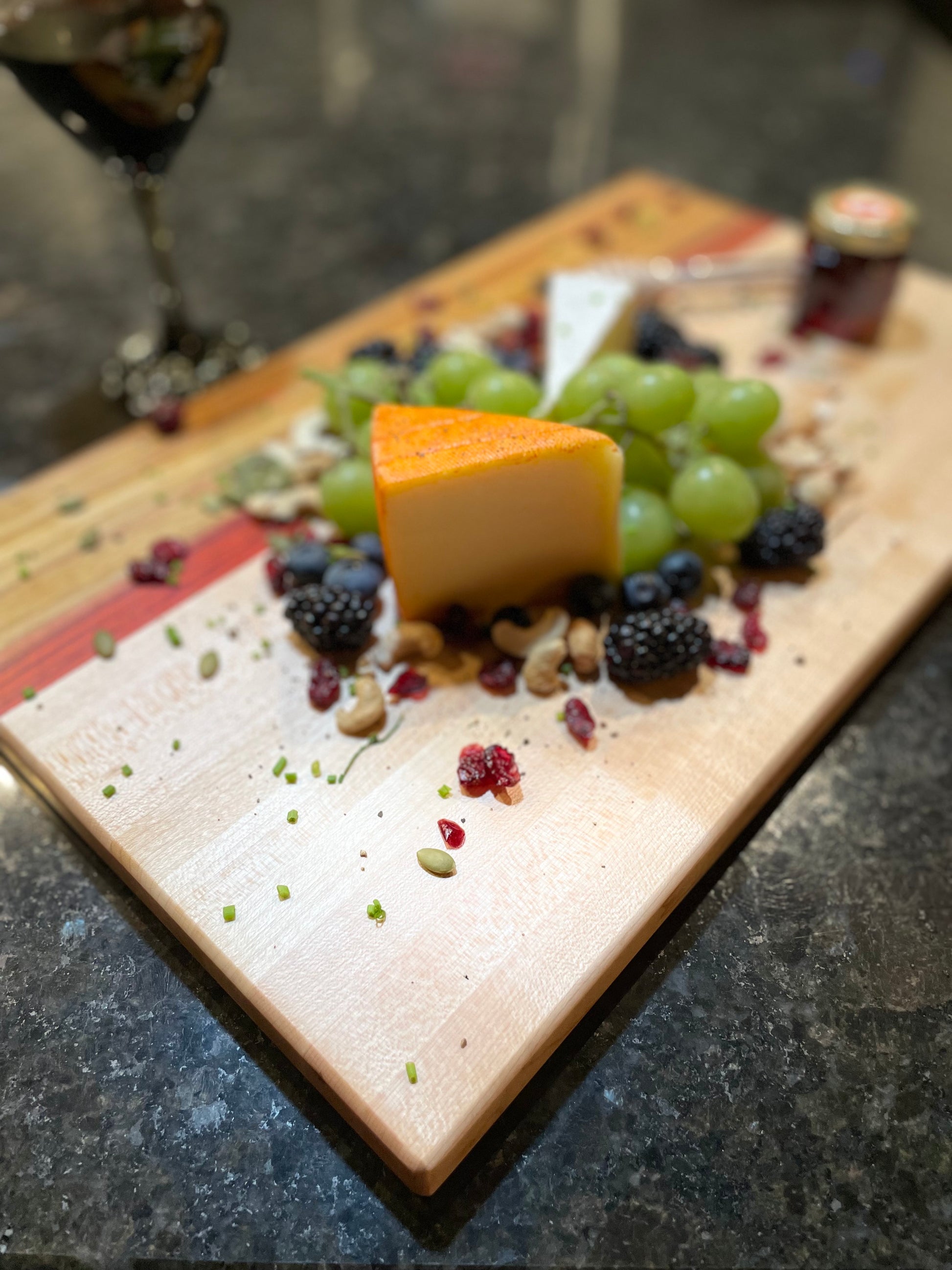 Maple, red zebrawood and canarywood edge grain charcuterie board featuring artisan cheese, grapes, berries and mixed nuts.