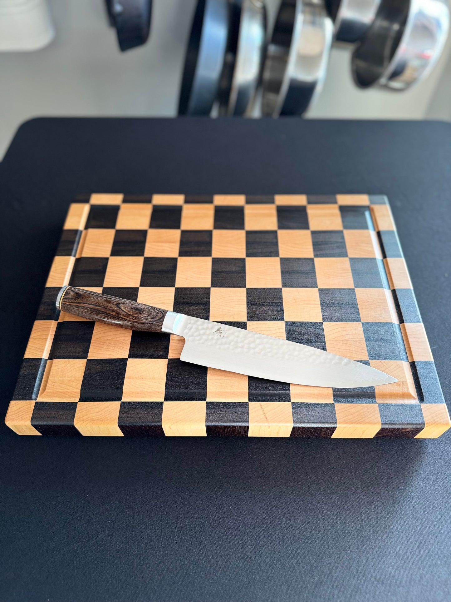 Handcrafted maple and walnut end grain checkerboard cutting board with a chef's knife for scale.