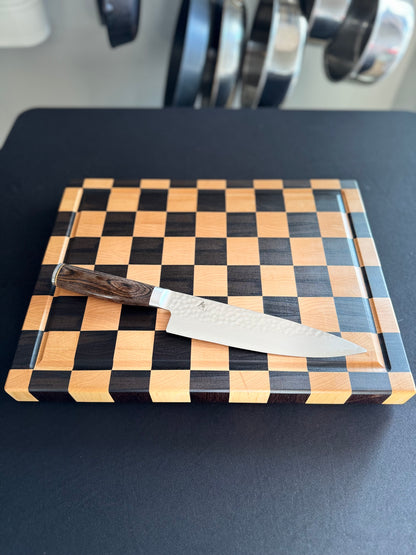 Handcrafted maple and walnut end grain checkerboard cutting board with a chef's knife for scale.
