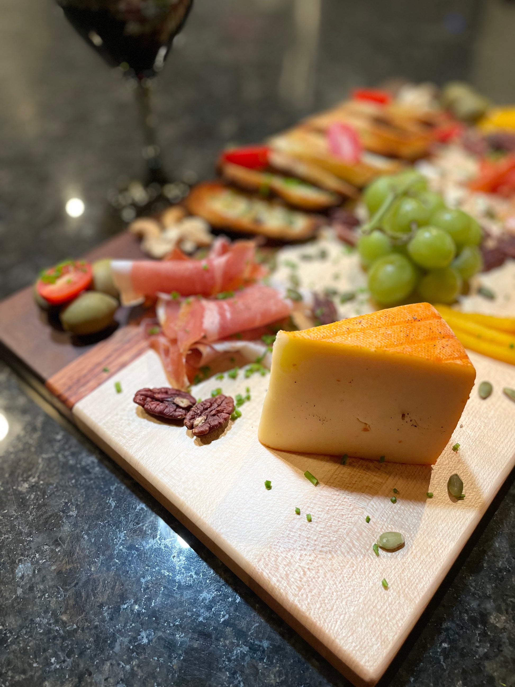 Maple, walnut and red zebrawood edge grain charcuterie board featuring artisan cheese, grapes, cured meats and toasted bread.