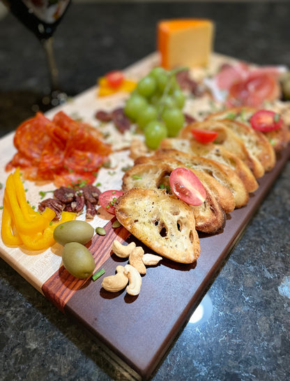 Maple, walnut and red zebrawood edge grain charcuterie board styled with artisan bread, cured meats, olives and vegetables.