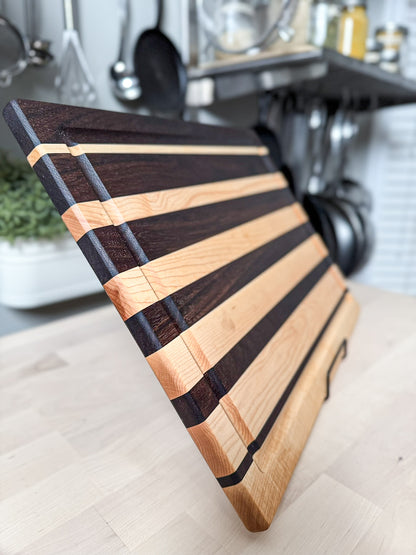 Angled view of a handcrafted maple and walnut striped edge grain cutting board.