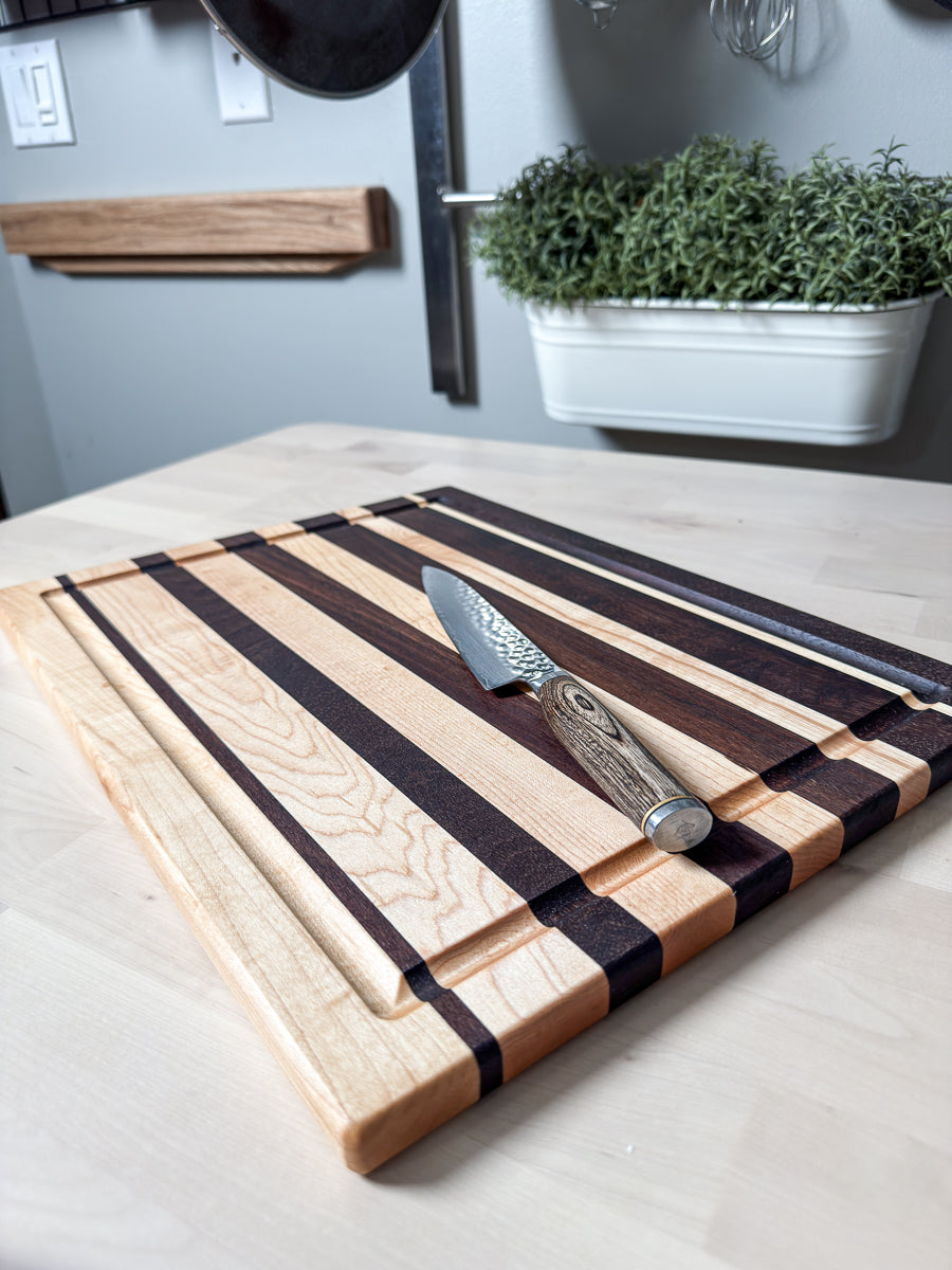 Maple and walnut striped edge grain cutting board displayed with a chef's knife.
