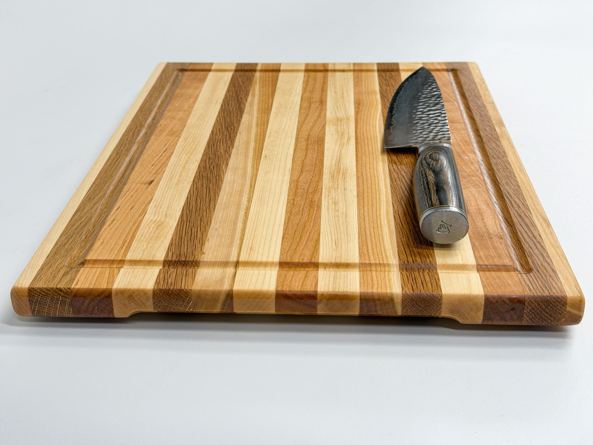 Low-angle view of handcrafted maple, white oak and cherry edge grain cutting board showing its striped design