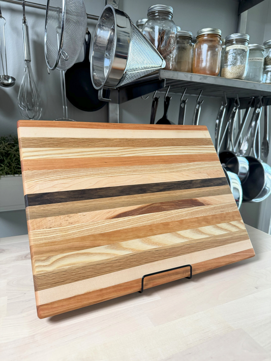 Handcrafted edge grain cutting board made from maple, white oak and cherry, displayed standing.