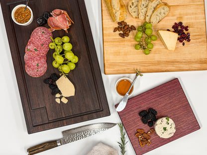 Overhead view of walnut, maple and purpleheart charcuterie boards filled with meats, cheese, fruit and bread.