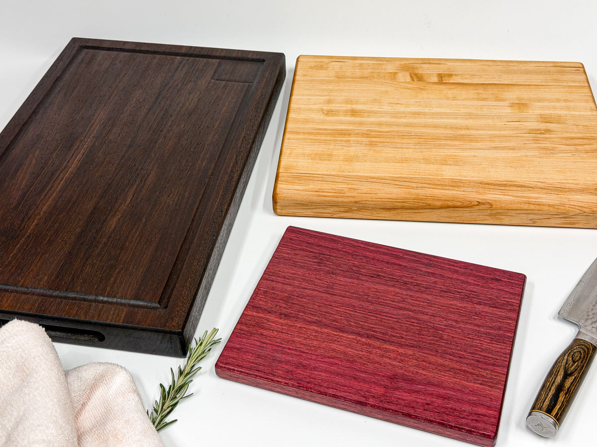 Walnut, maple and purpleheart cutting boards arranged with a knife and linen towel.