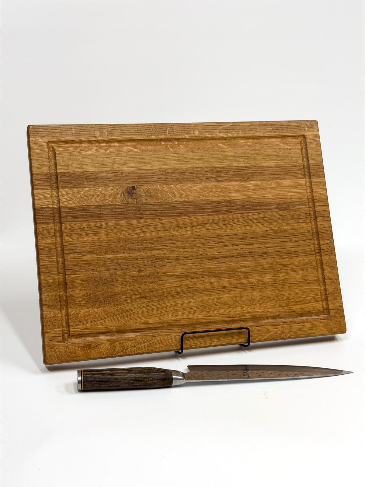 Light-colored white oak wood cutting board with a juice groove, displayed with a chef’s knife.