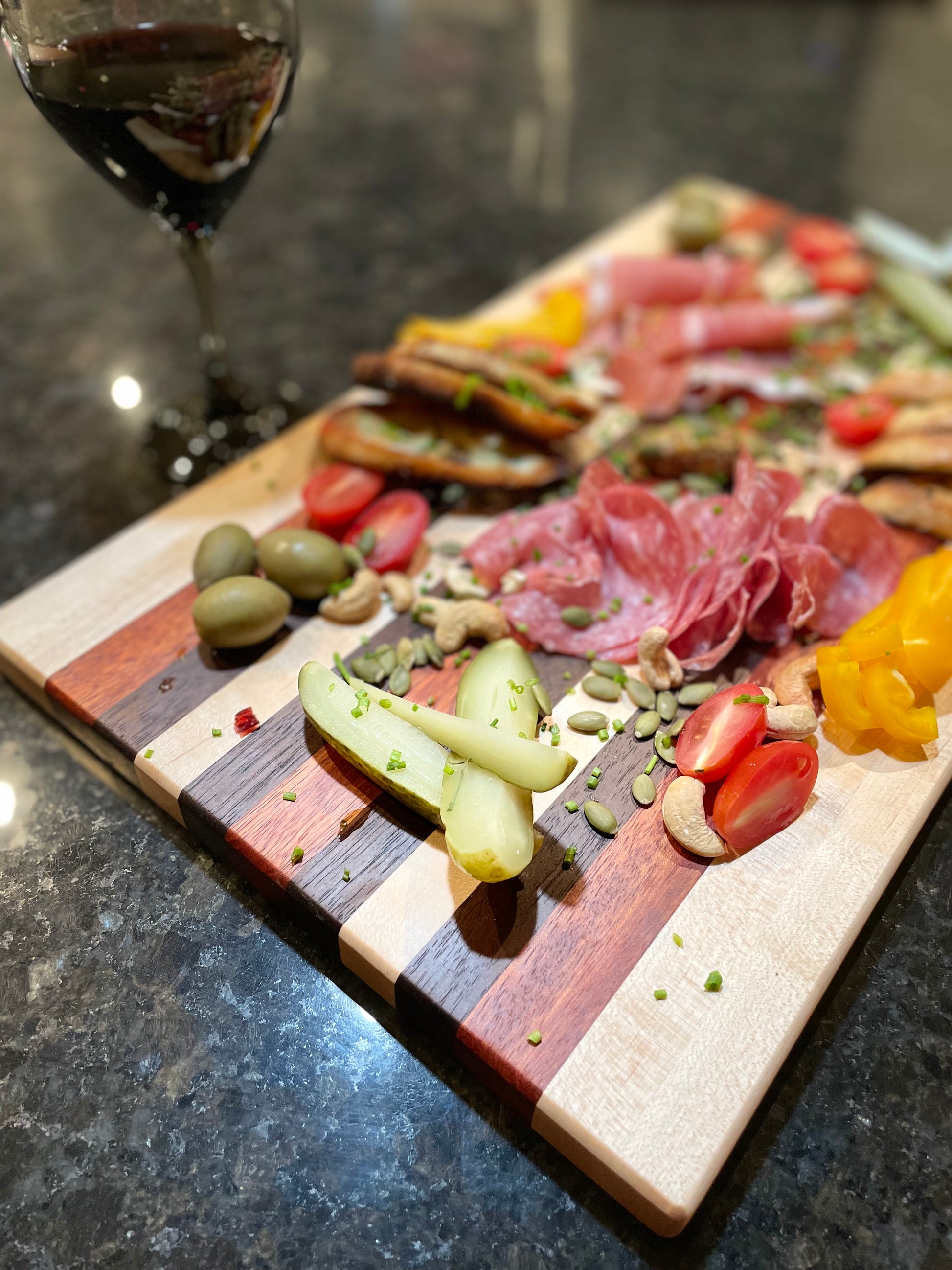 custom edge grain charcuterie red zebrawood maple walnut, side/top view, cured meats, vegetables, olives and a glass of red wine.