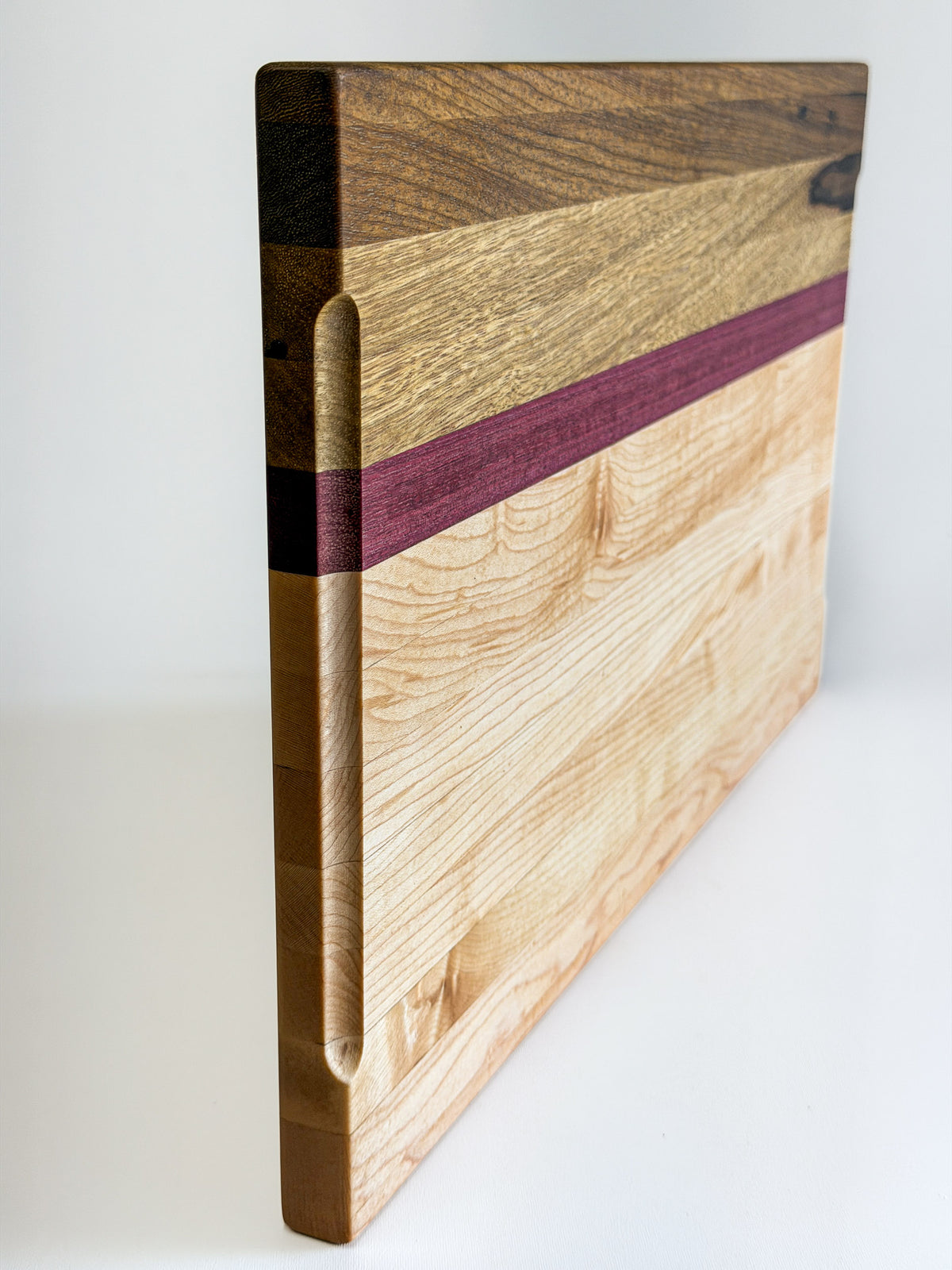 Side view showing the thickness and layered edge of a maple, purpleheart and black limba charcuterie board.