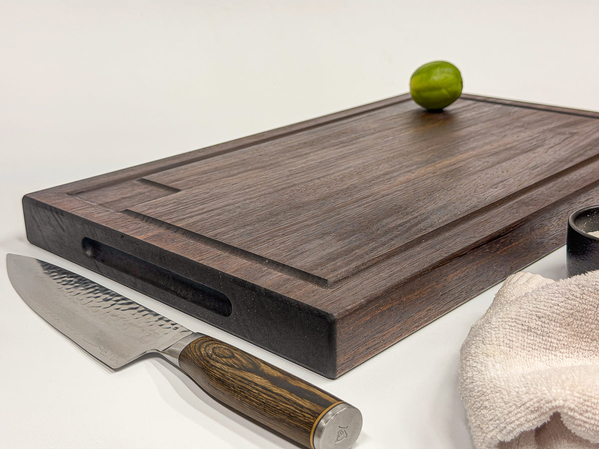 Walnut edge-grain BBQ cutting board with routed drip tray, lime, knife and linen towel.