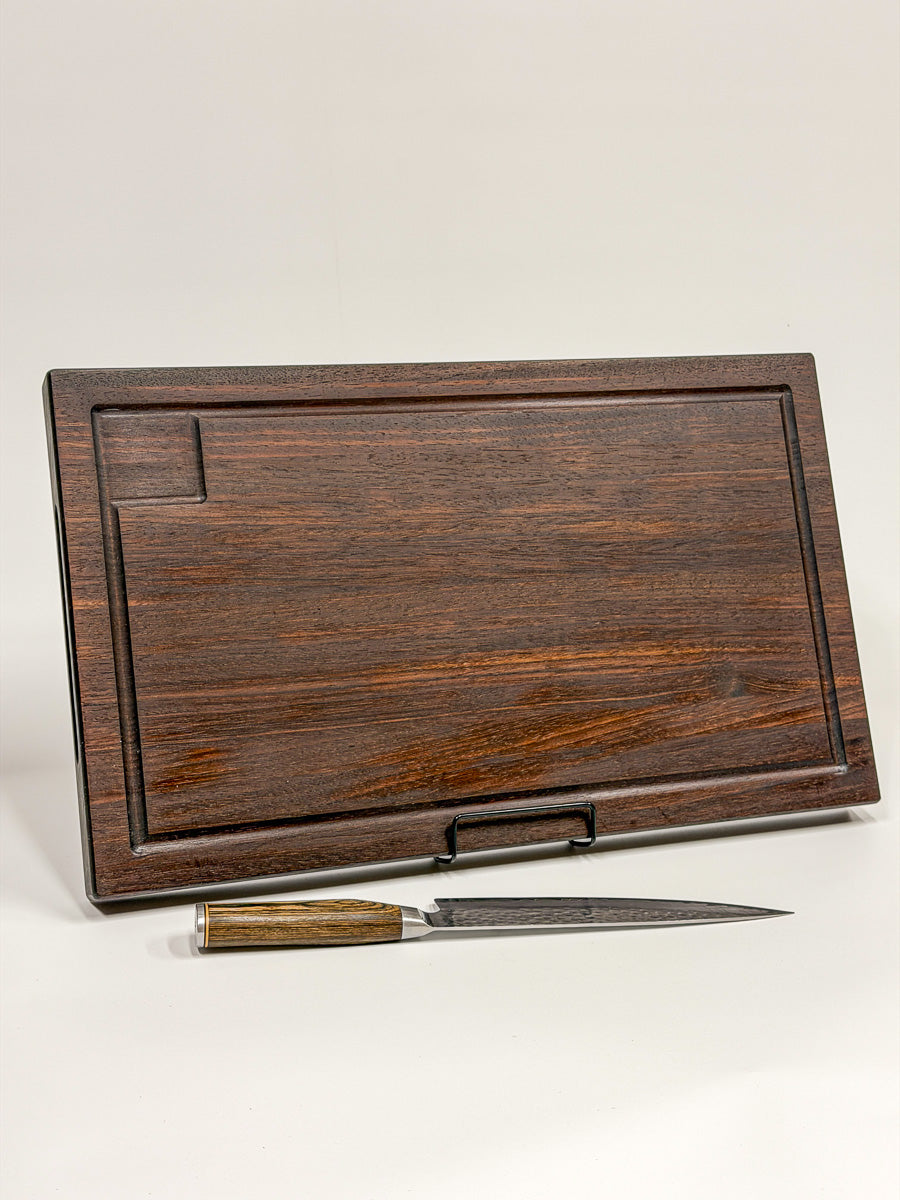 Walnut edge-grain BBQ cutting board displayed upright with routed drip tray and knife.
