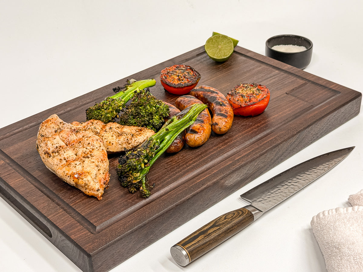 Walnut edge-grain BBQ cutting board with grilled chicken, sausages, broccolini and tomatoes.