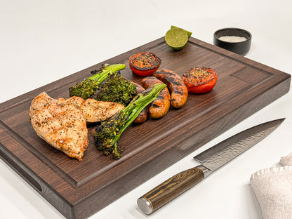 Walnut edge-grain BBQ cutting board with grilled chicken, sausages, broccolini and tomatoes.
