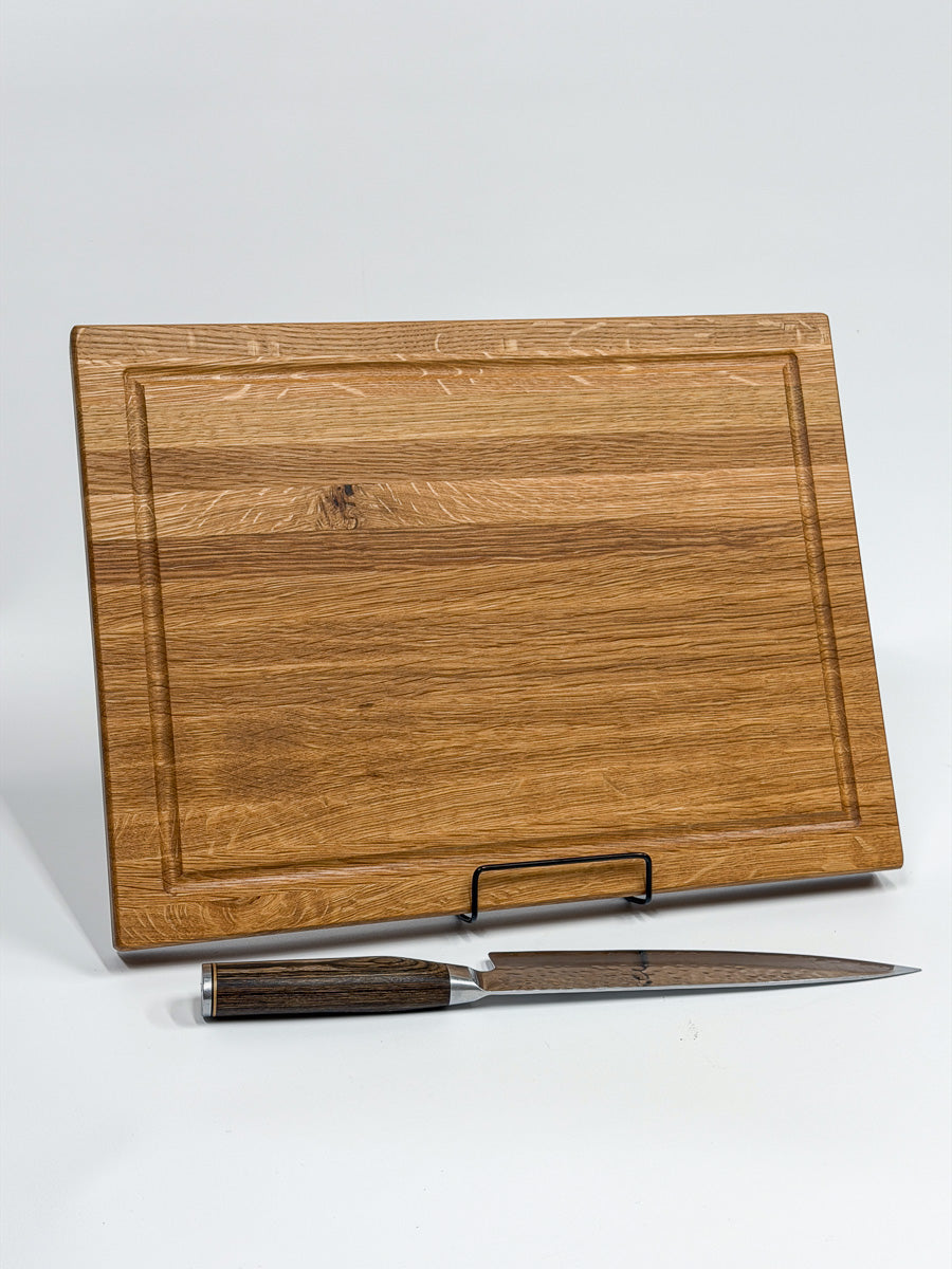 Portrait view of a handcrafted white oak cutting board with chef's knife.