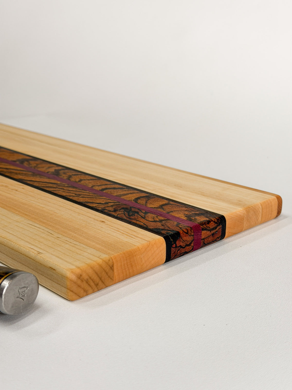 Close-up of the Zephyr cutting board’s rounded maple edge and contrasting zebrawood and purpleheart layers.