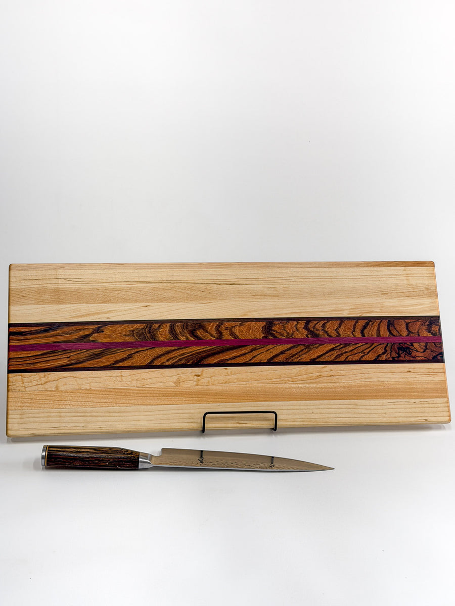 Striped maple, zebrawood, and purpleheart cutting board displayed with a chef’s knife.