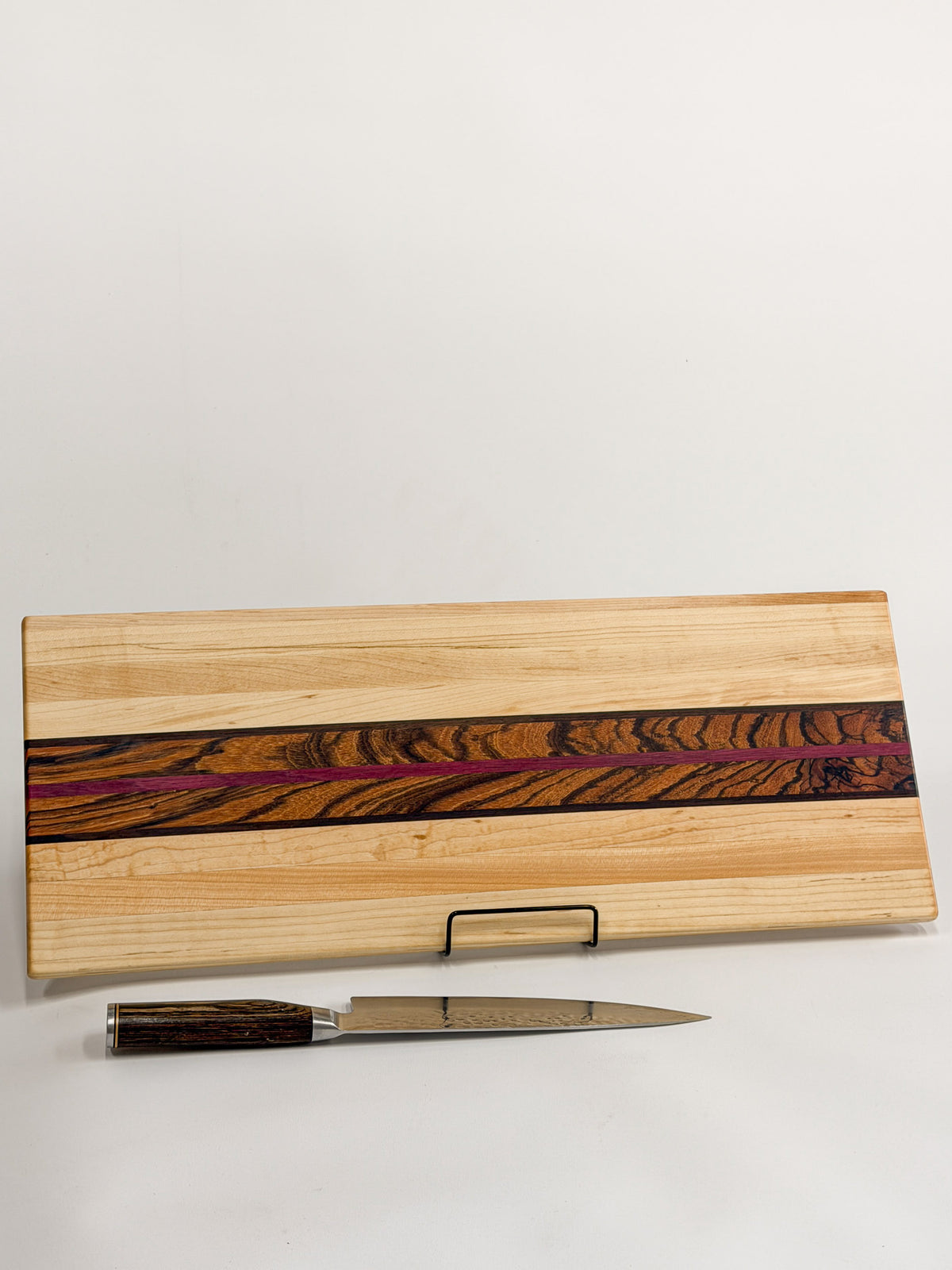 Zephyr cutting board made from maple with a zebrawood center and purpleheart accent, displayed with a kitchen knife.